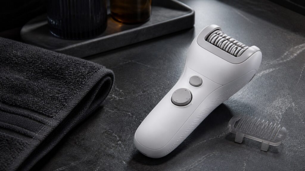 Robust unbranded epilator with broad tweezer head and trimming comb on a dark bathroom counter